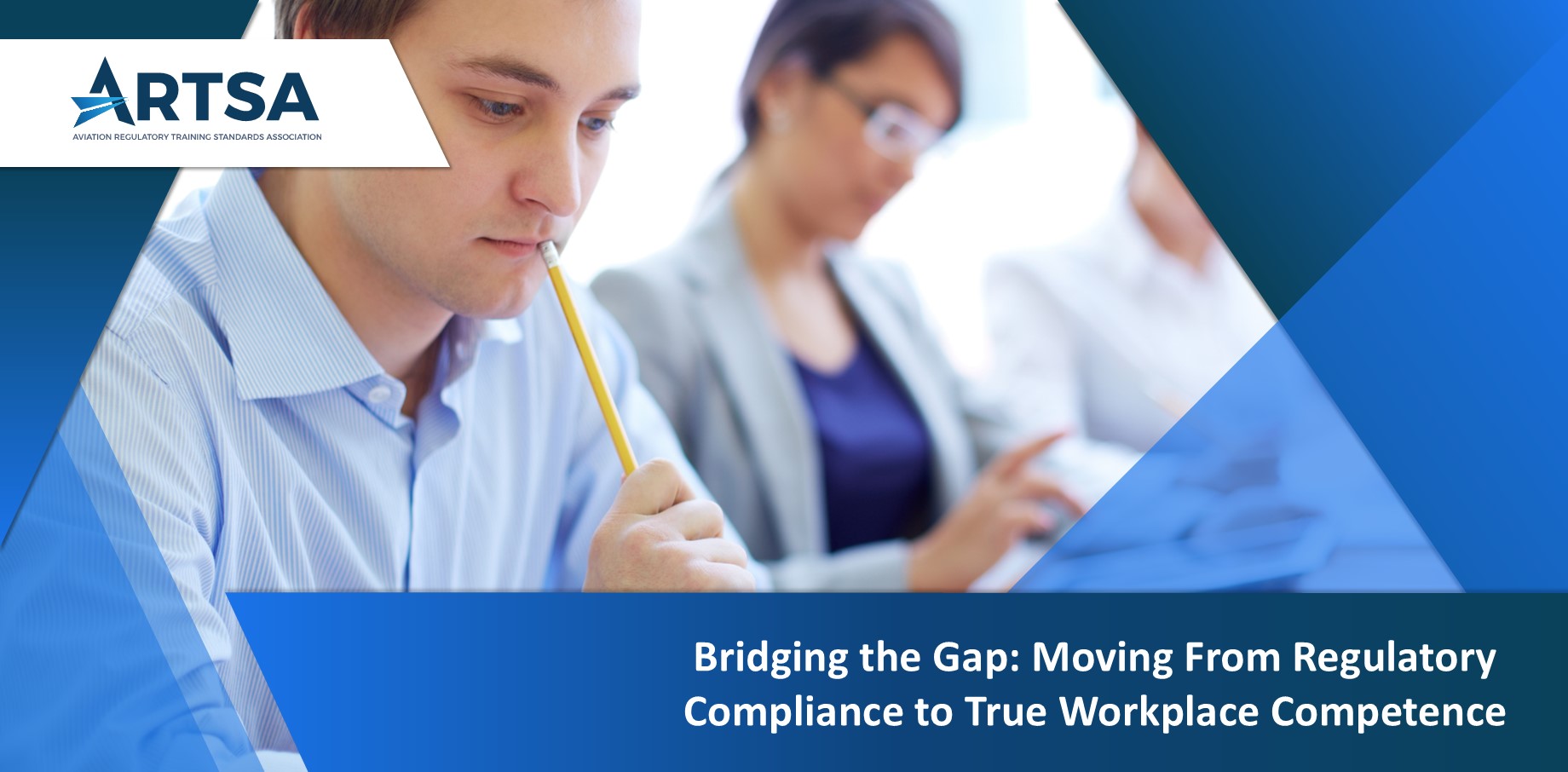 A person in a training classroom thoughtfully holding a pencil, with other participants working in the background.